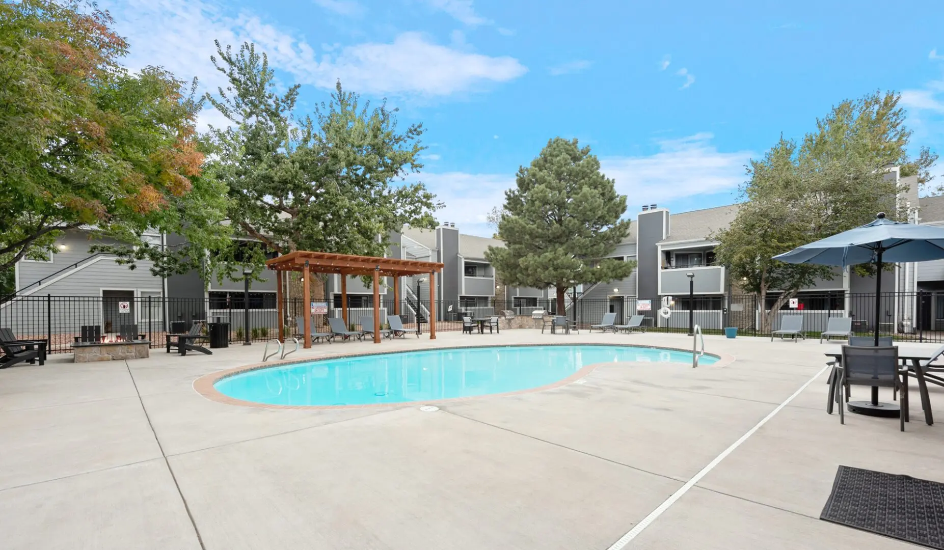 A pool with a wooden pergola and trees in the background.